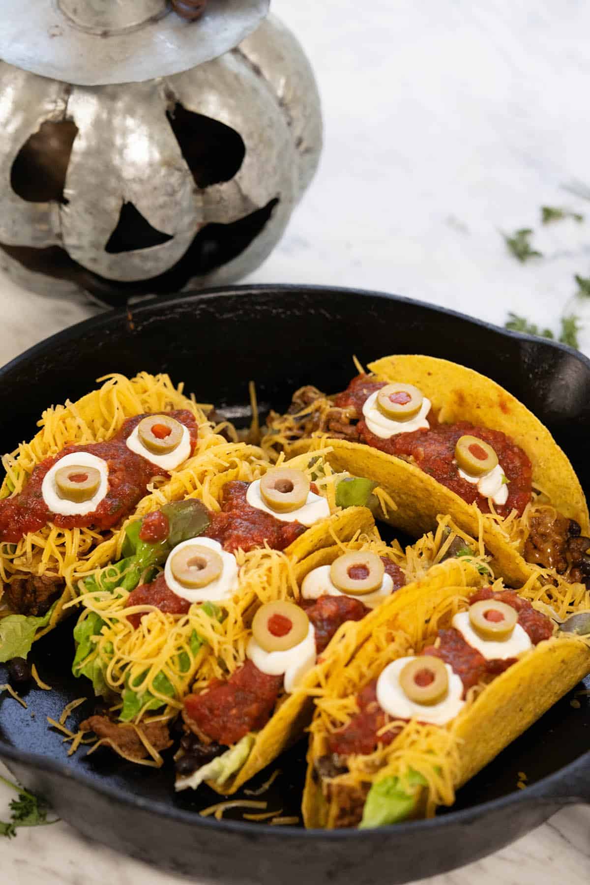 Crispy tacos in a skillet topped with sour cream and olives that look likes eyes. They are perfect for Halloween.