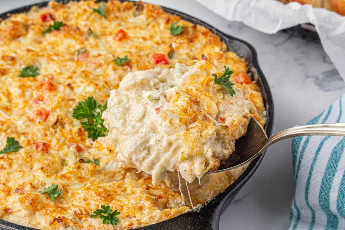 Hot crab dip in a skillet with a spoon taking out a scoop.