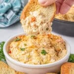 Louisiana Hot Crab Dip in a bowl with a toasted baguette dipping out a scoop.