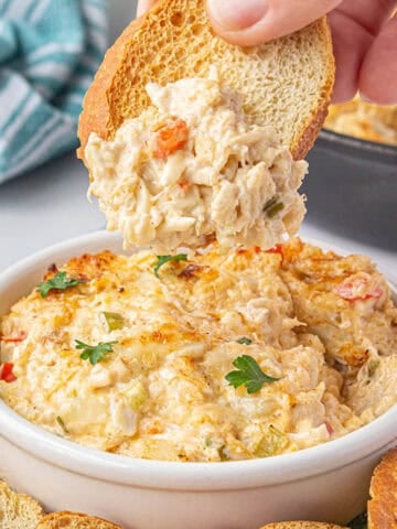 Louisiana Hot Crab Dip in a bowl with a toasted baguette dipping out a scoop.