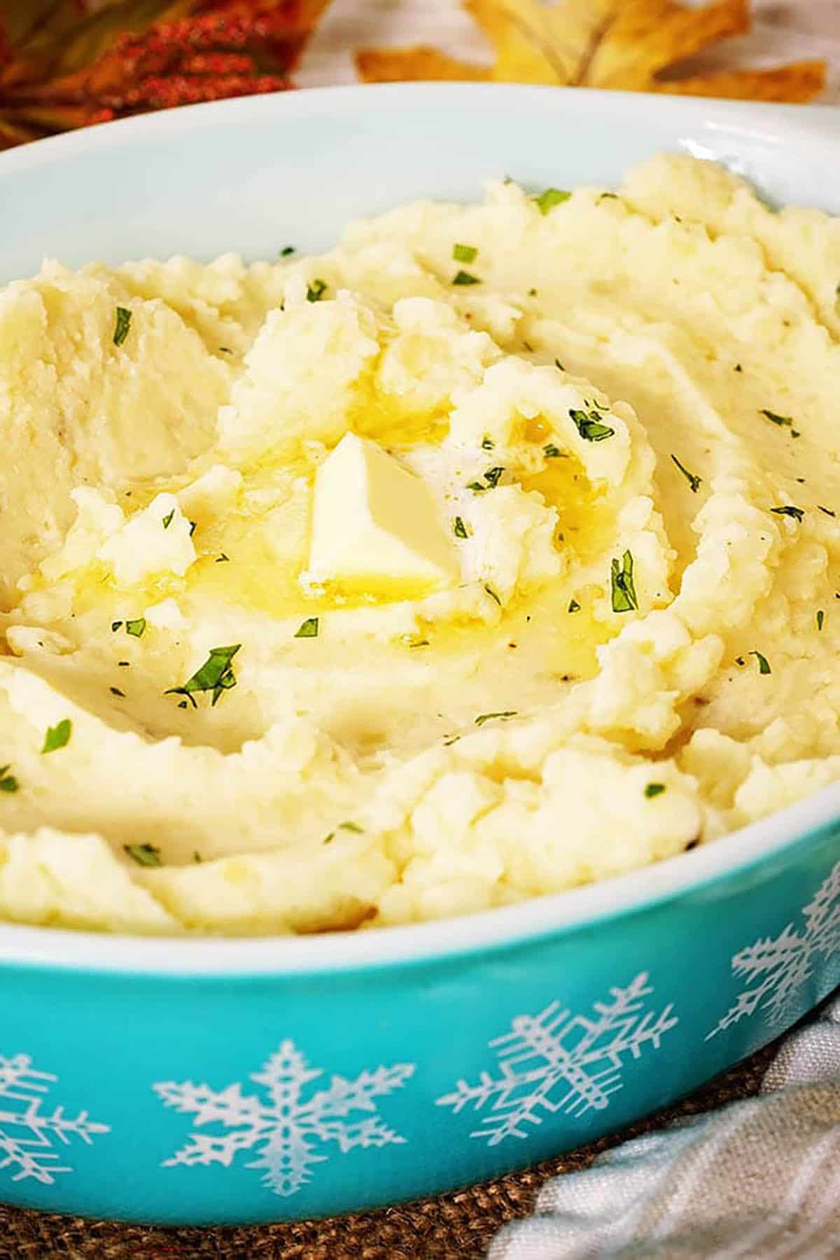 Mashed cauliflower and potatoes in a pretty green bowl, topped with melted butter.