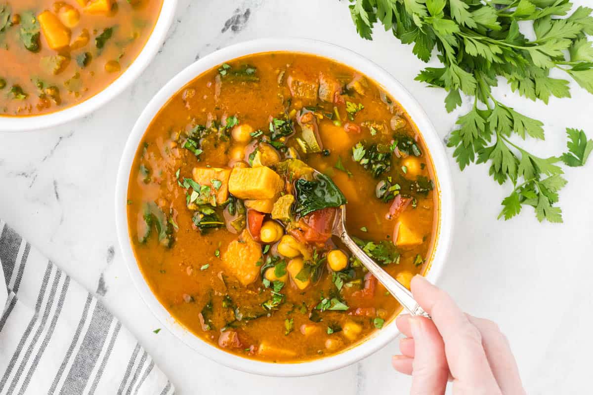 Two bowls filled with sweet potato soup, with a hand reaching in to get a spoonful of soup.