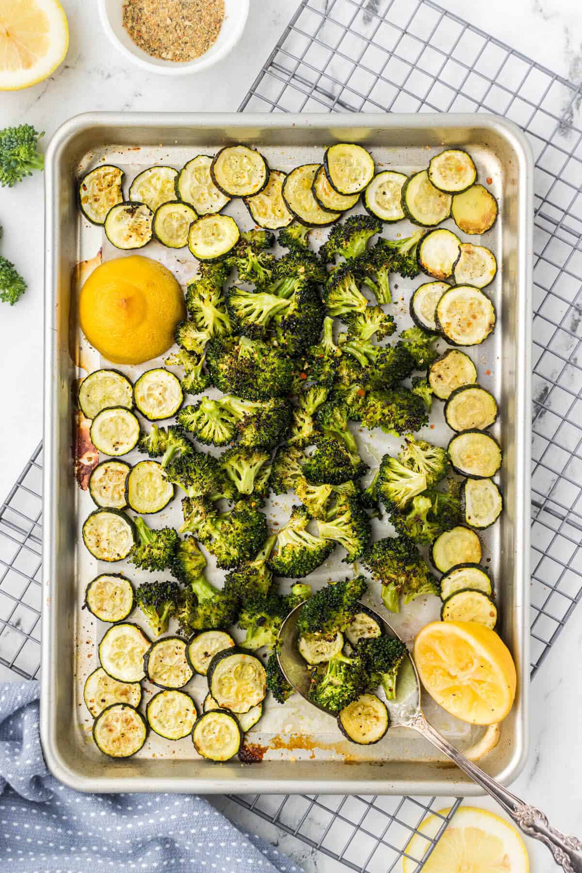 Roasted broccoli and zucchini on a sheet pan, with a serving spoon on the side to dish up a serving.