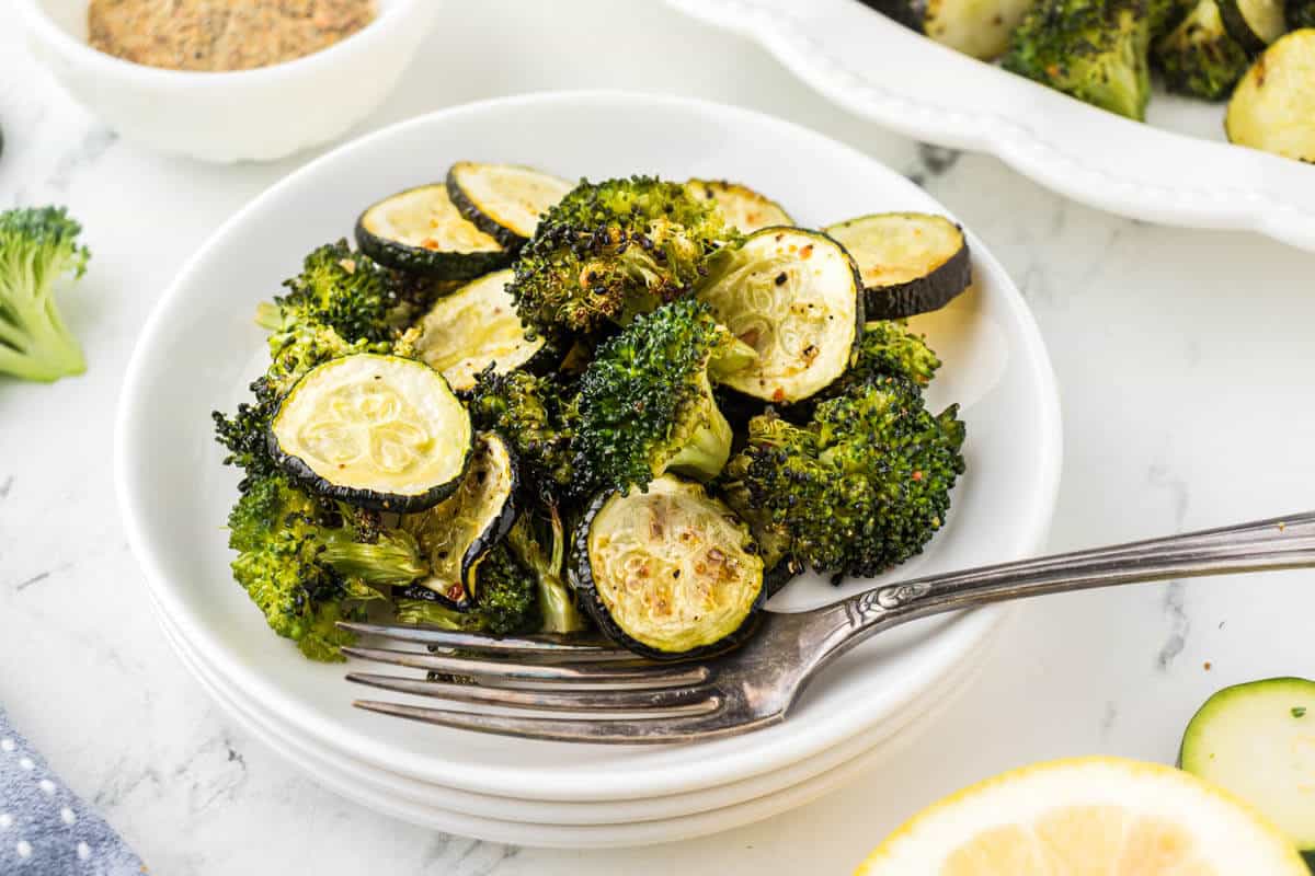 Cooked vegetables on a plate with a fork. The sheet pan, filled with roasted veggies is in the background.