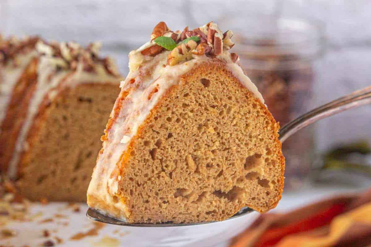 A slice of sweet potato bundt cake on a serving spatula, with the rest of the cake in the background.