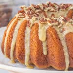 Sweet potato bundt cake on cake stand. The cake has been drizzled with a maple icing and topped with chopped pecans.