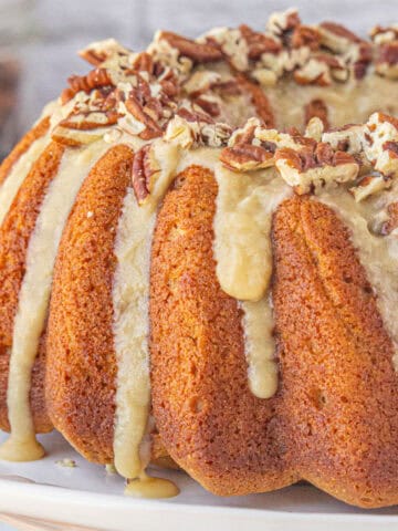 Sweet potato bundt cake on cake stand. The cake has been drizzled with a maple icing and topped with chopped pecans.