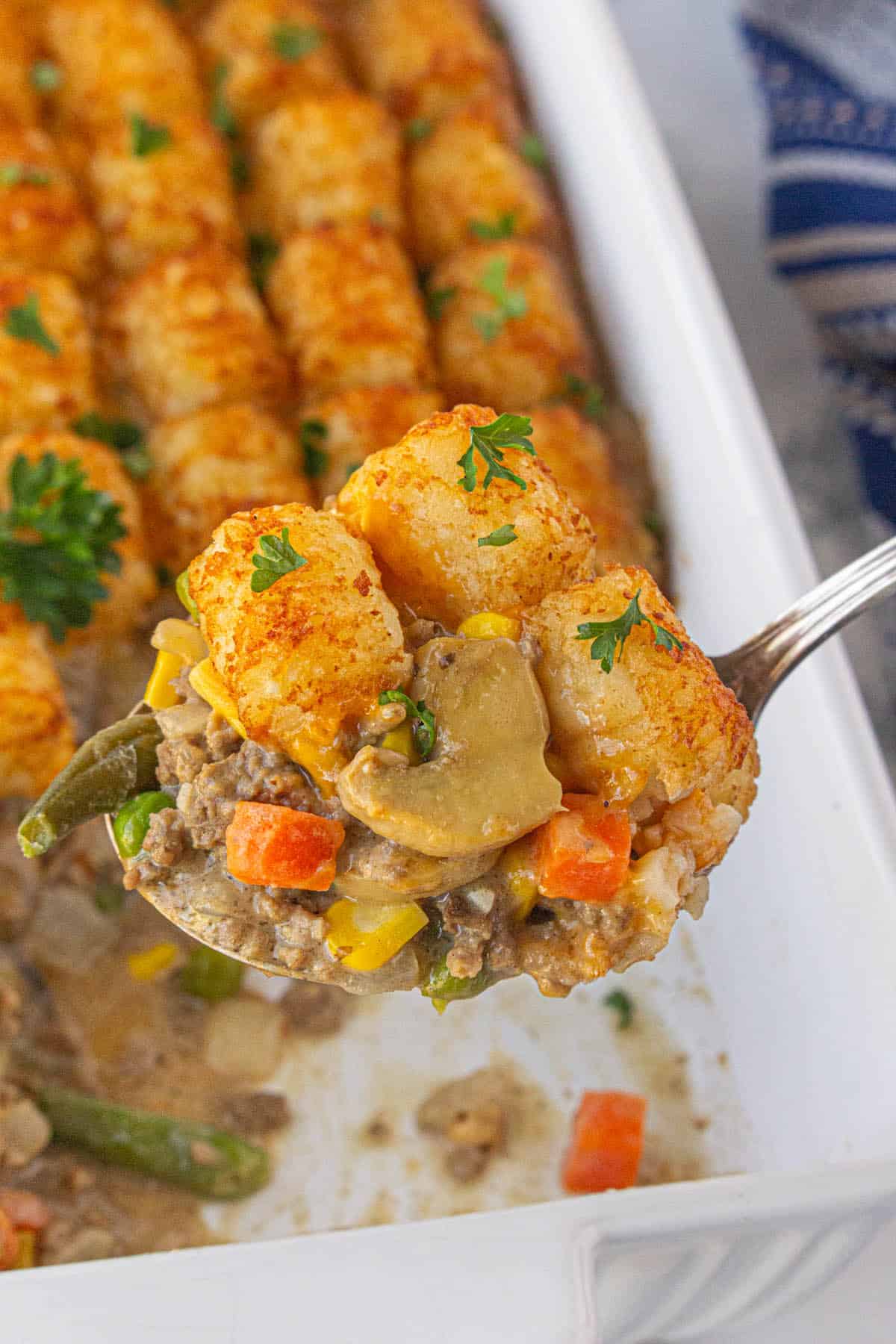 Tater tot shepherds pie casserole in a baking dish, with a spoon taking a big scoop to serve.