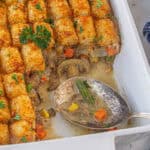 Tater tot shepherds pie casserole in a baking dish. A spoon has already removed a serving and it's laying in the casserole.