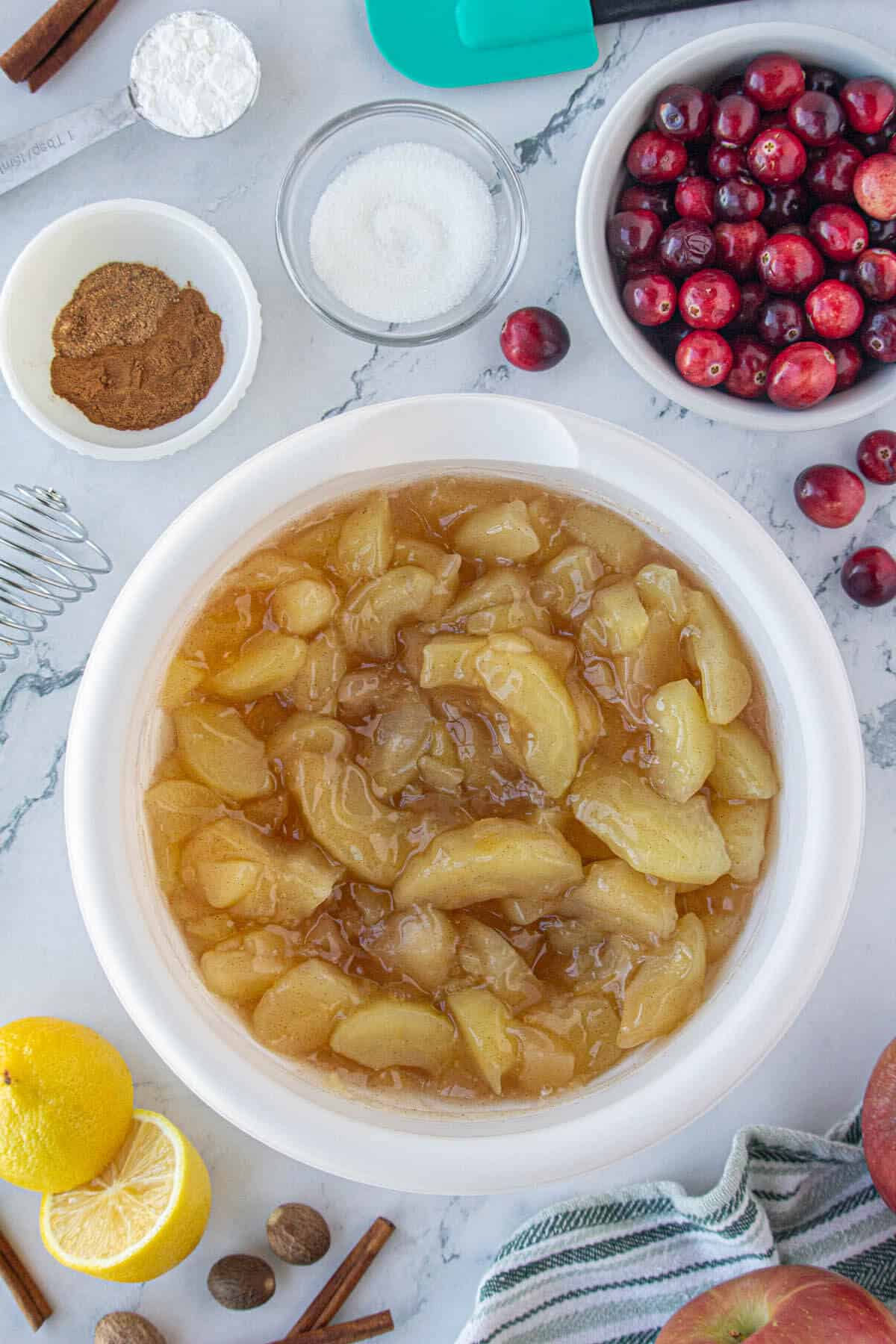 Apple pie filling in a large white bowl, surrounded by the other ingredients needed to make the recipe.