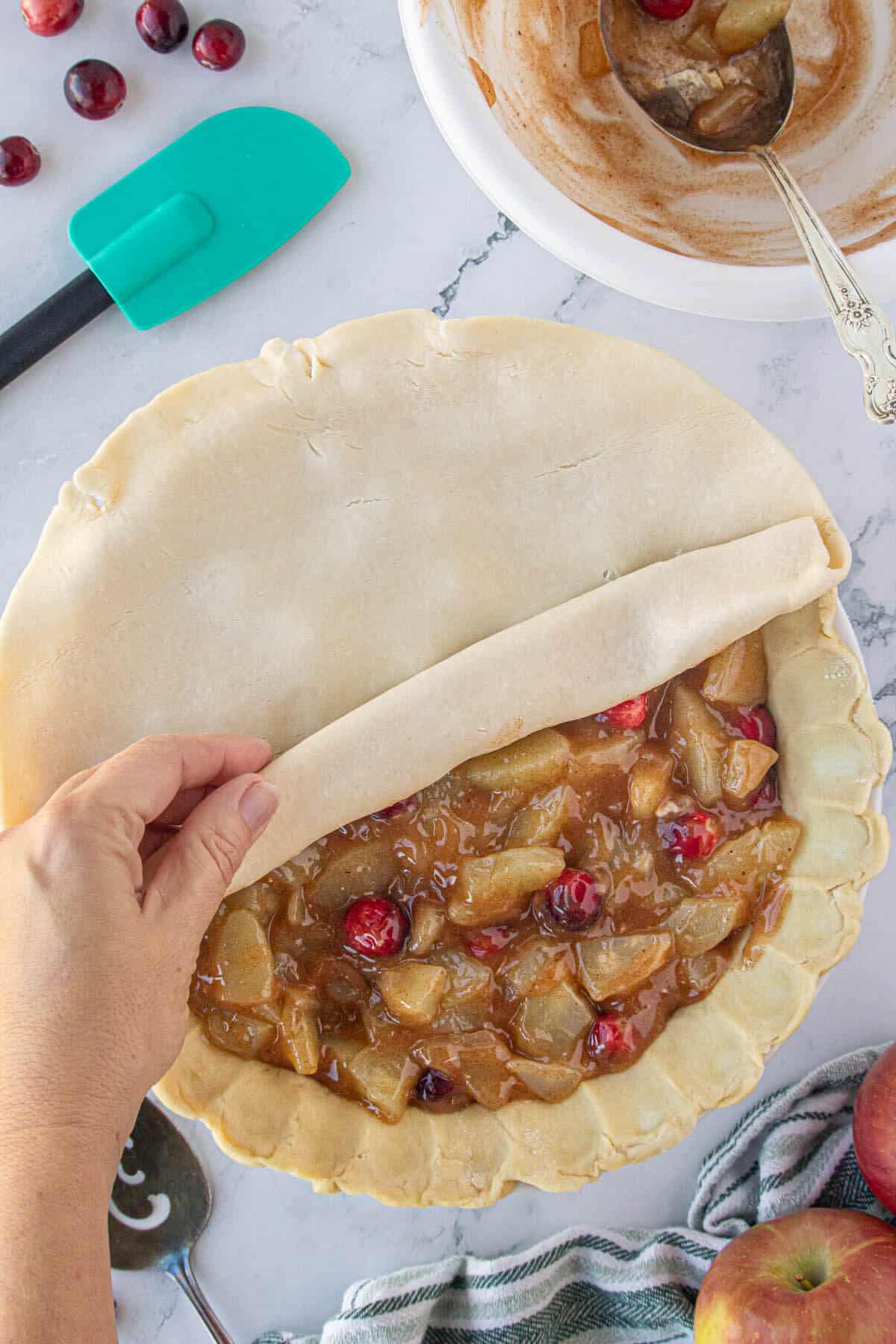 The top of a pie crust being rolled onto an apple pie.