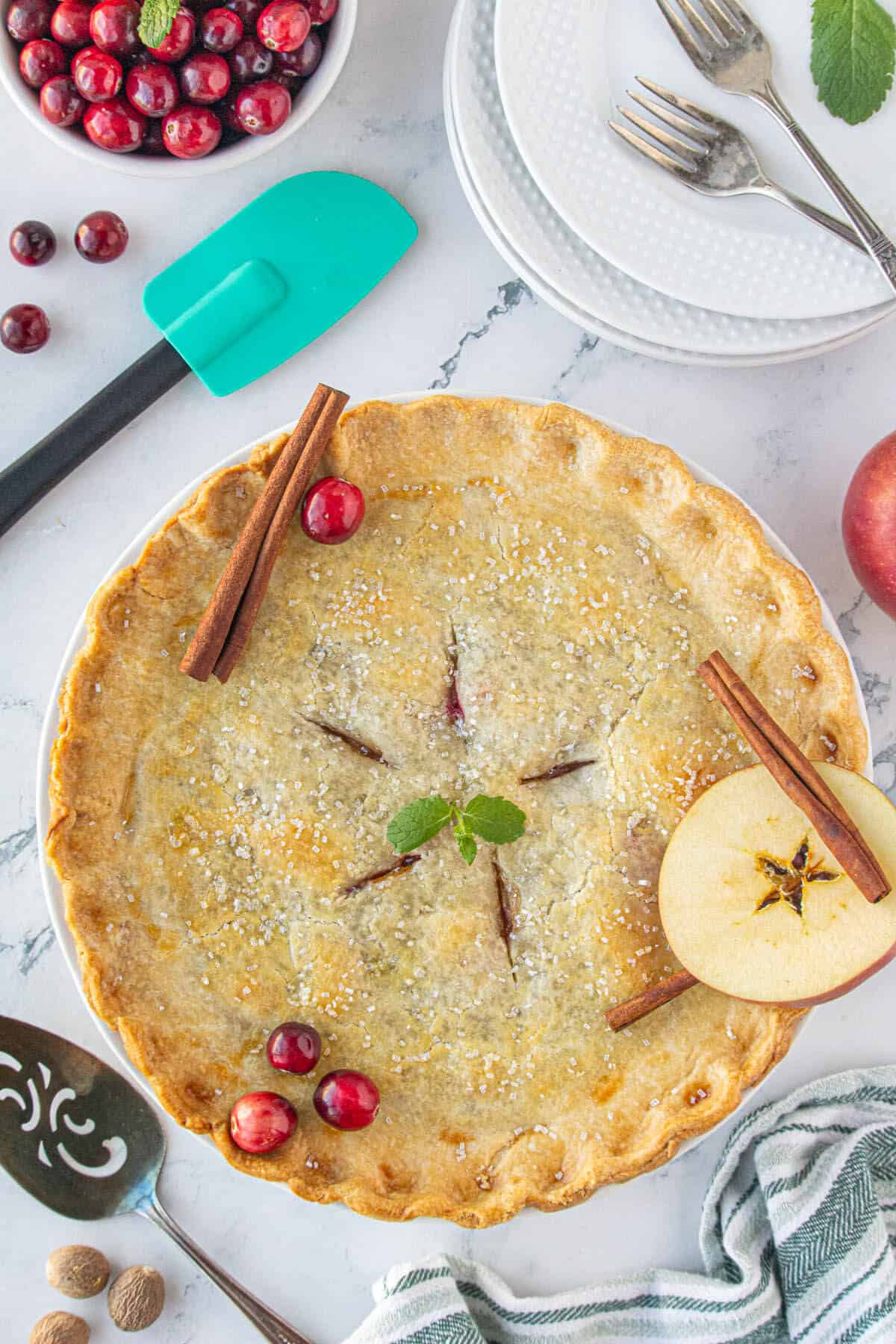 A baked apple pie with cranberries on a platter ready to slice.