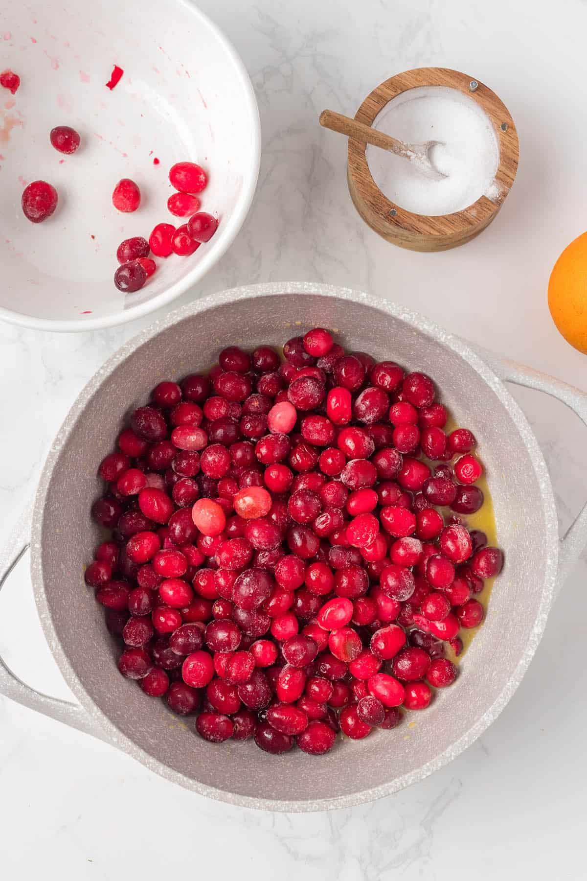 Whole cranberries orange juice and apples in a saucepan.