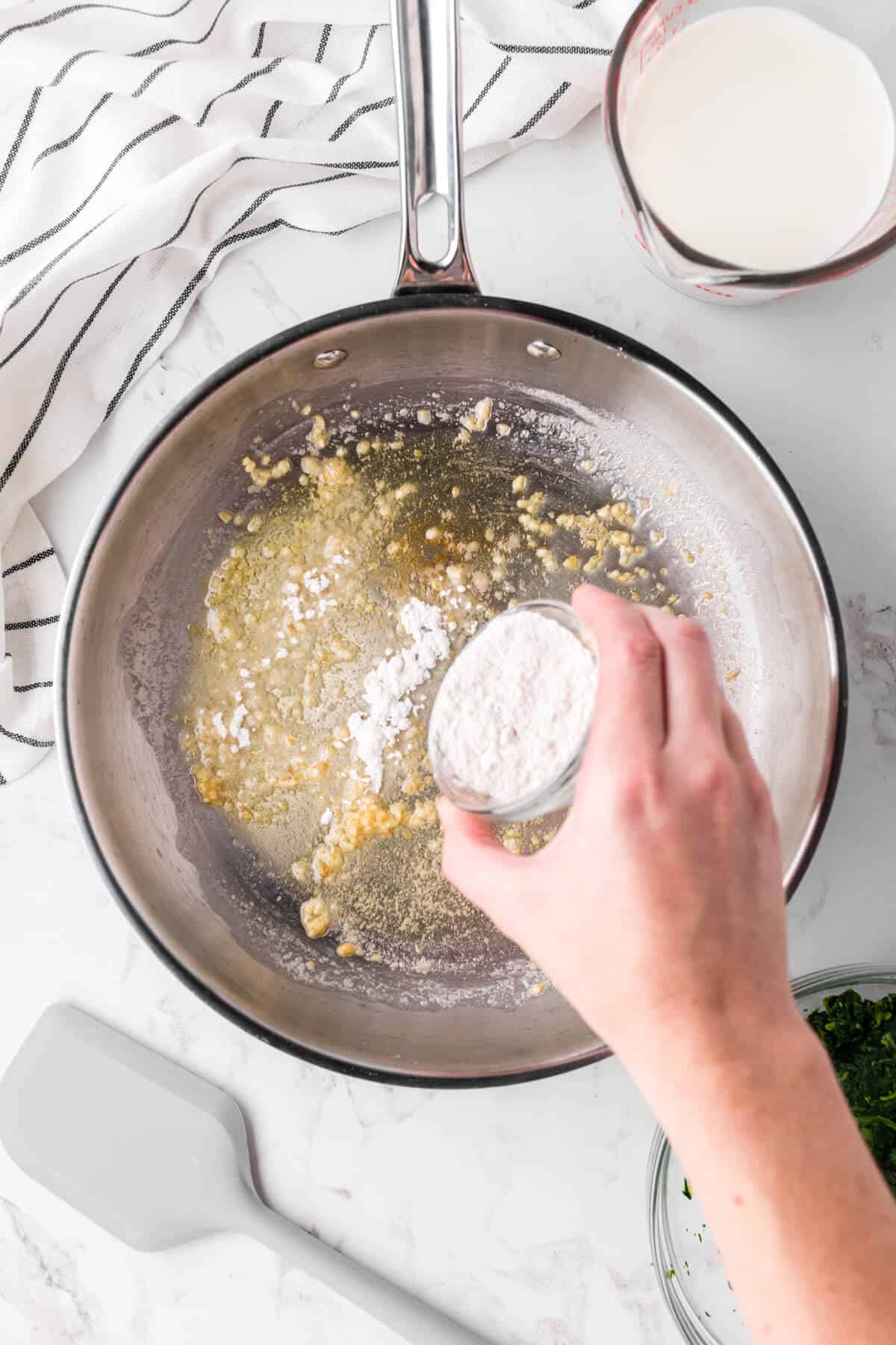 Flour being sprinkled over butter and garlic in a skillet.