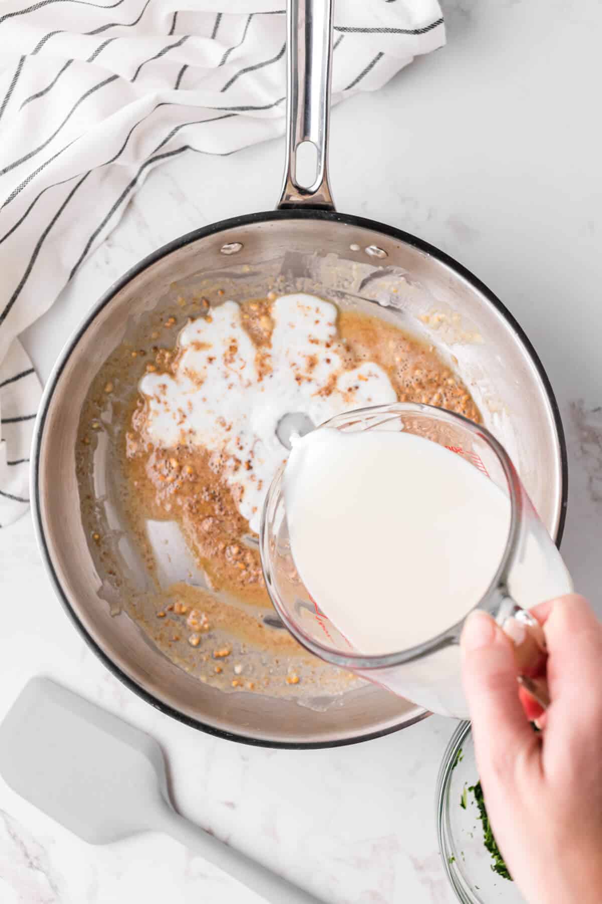 Milk being poured into a roux in a skillet.