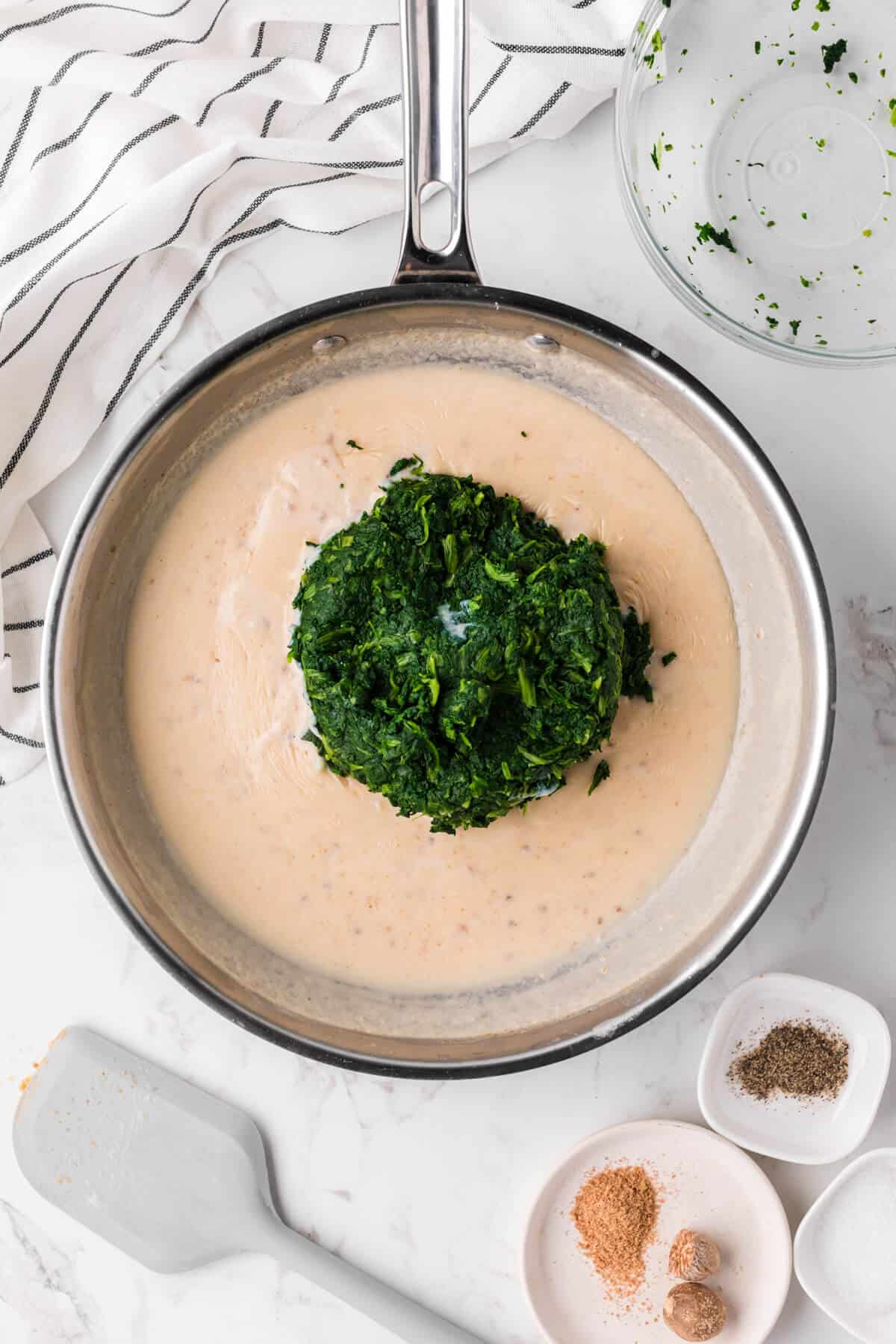 Spinach added into a skillet with a cream sauce.