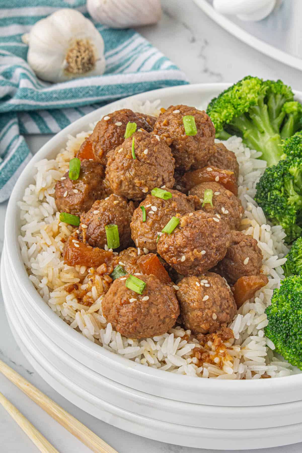 Teriyaki meatballs on a plate over rice, serve with broccoli.