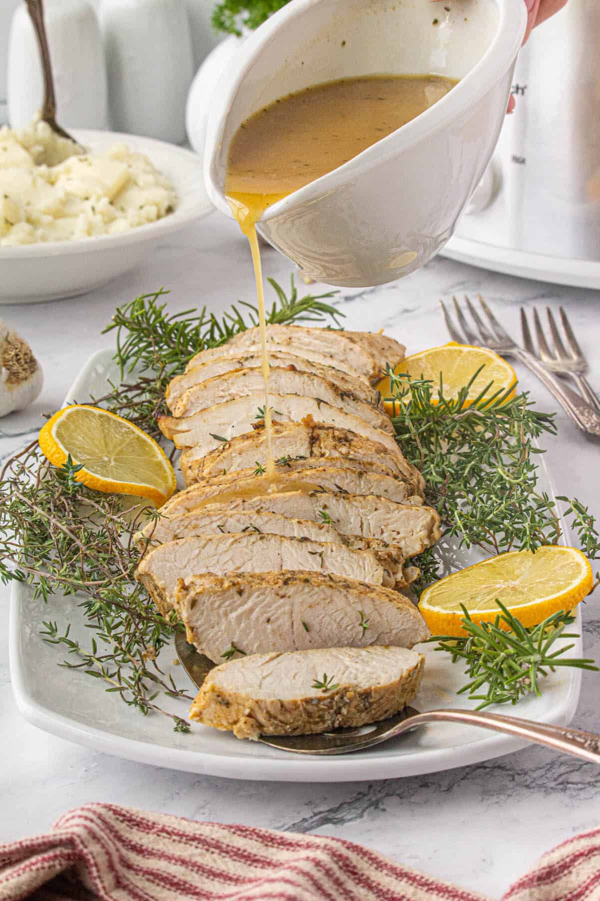 Sliced turkey tenderloin on a serving platter with a crockpot in the background. Gravy is being poured over the slices of turkey.