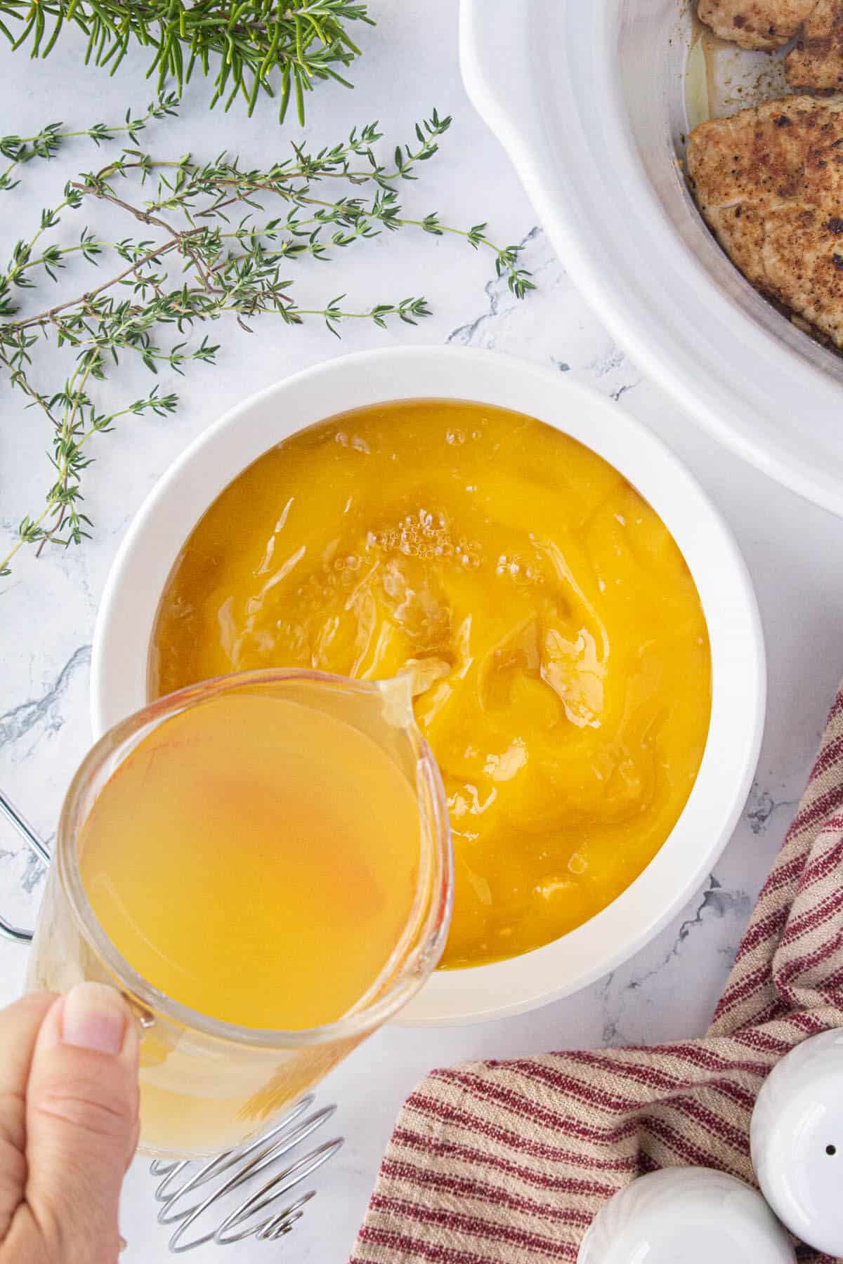 Chicken stock pouring into a bowl filled with cream of chicken soup.