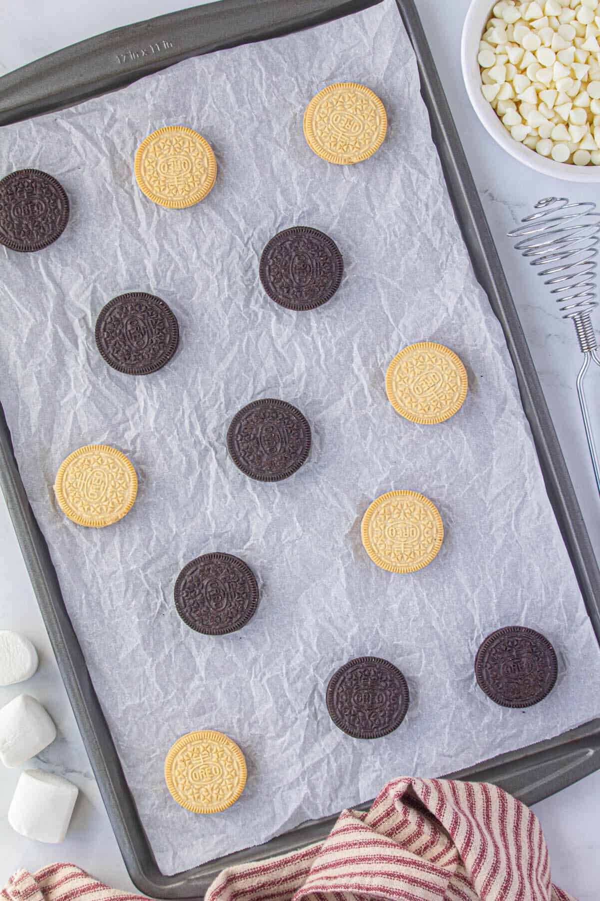 Chocolate and vanilla Oreos laying on parchment paper on a sheet pan.