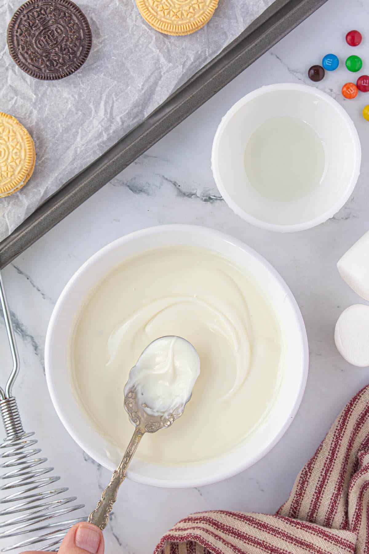 White chocolate melted in a small white bowl, being stired by a spoon.