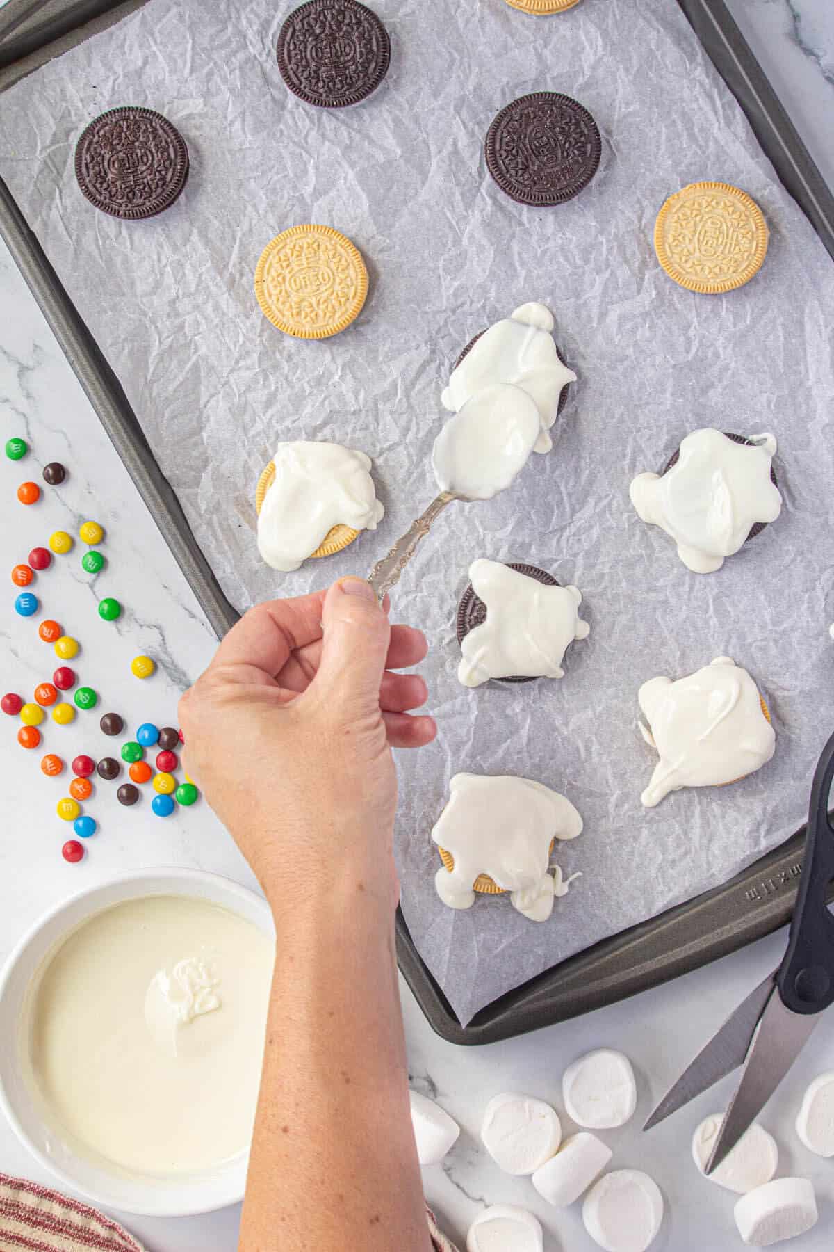 Melted white chocolate being spooned over the top over Oreo cookies and drizzled over the sides of the cookies.