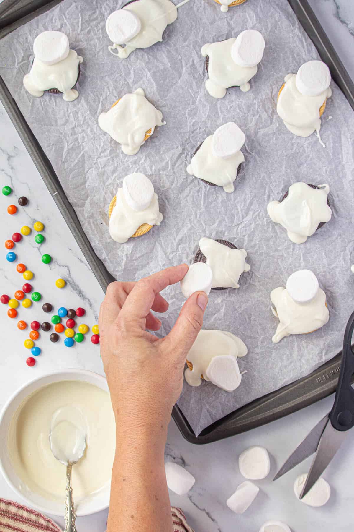 Sliced marshmallows being placed on top of the melted chocolate on the cookies.