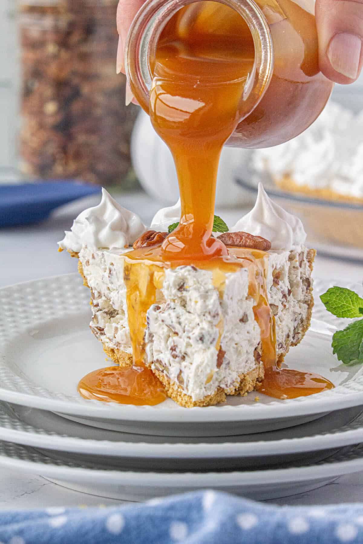 A slice of pecan cream pie on a plate being drizzled with caramel sauce.