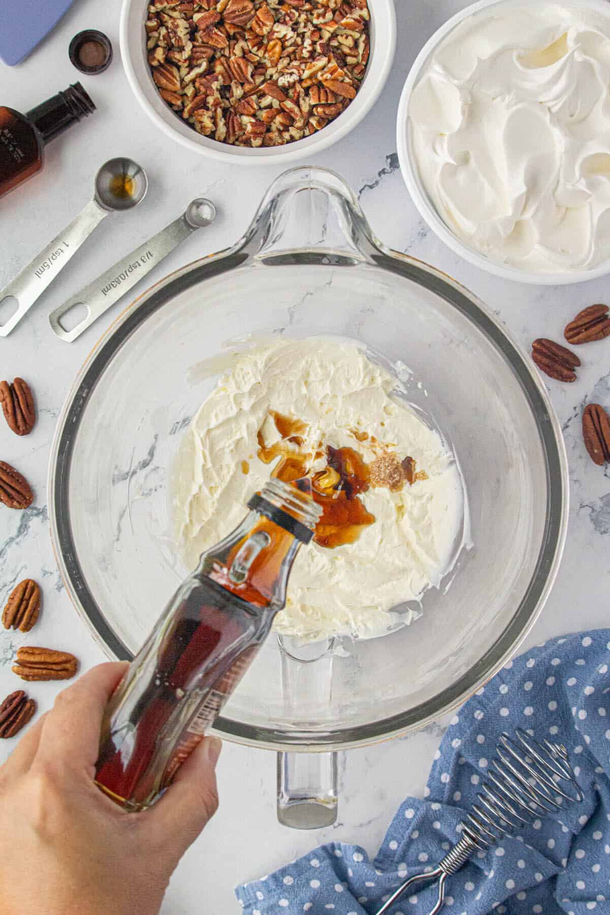 Maple syrupd and vanilla added to whipped cream cheese in a mixing bowl.