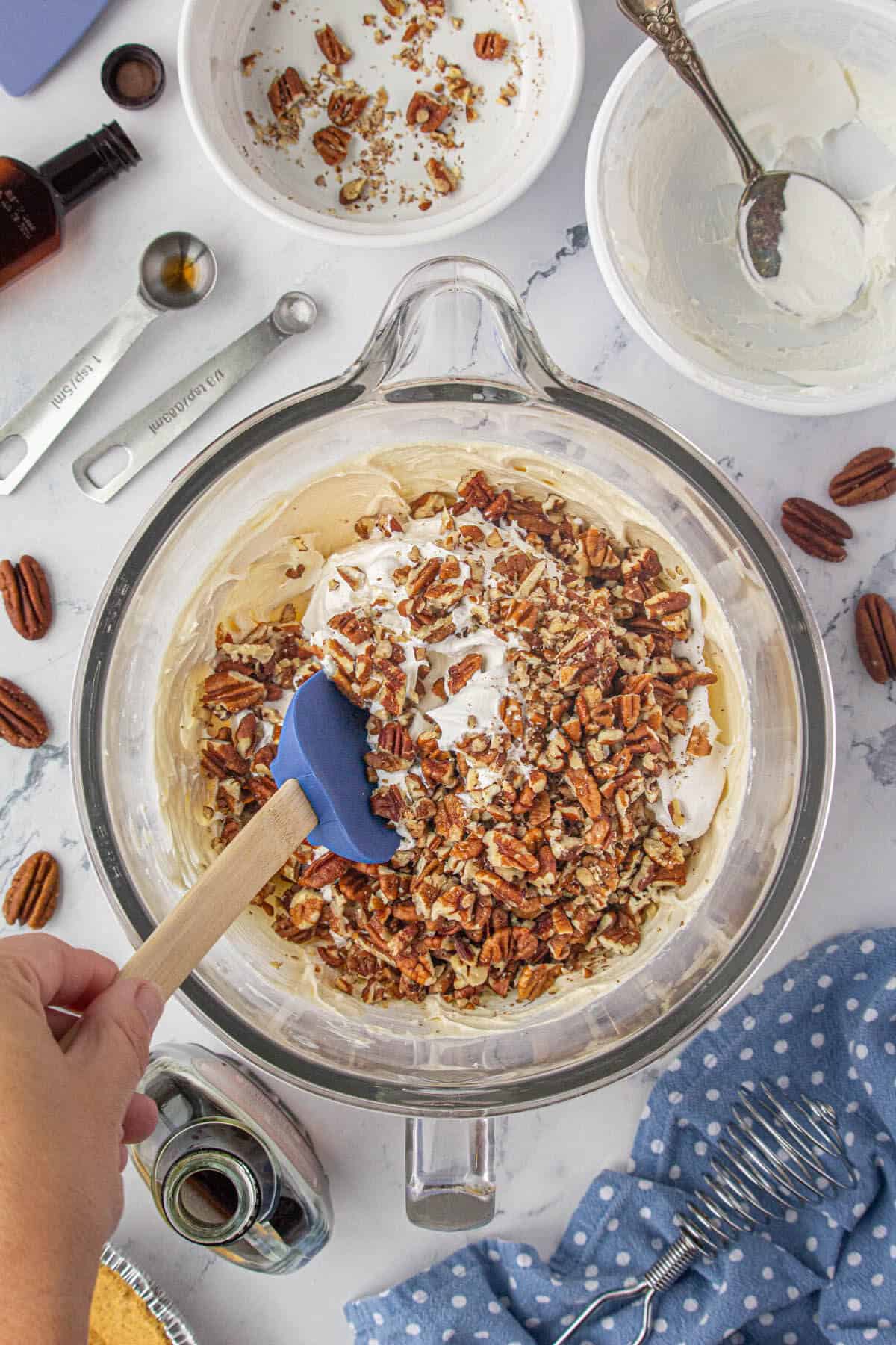 Chopped pecans folded into cream cheese in a mixing bowl.