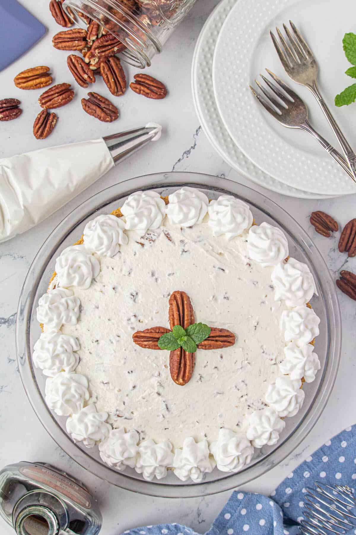 Pie being decorated with whipped cream and pecan halves.