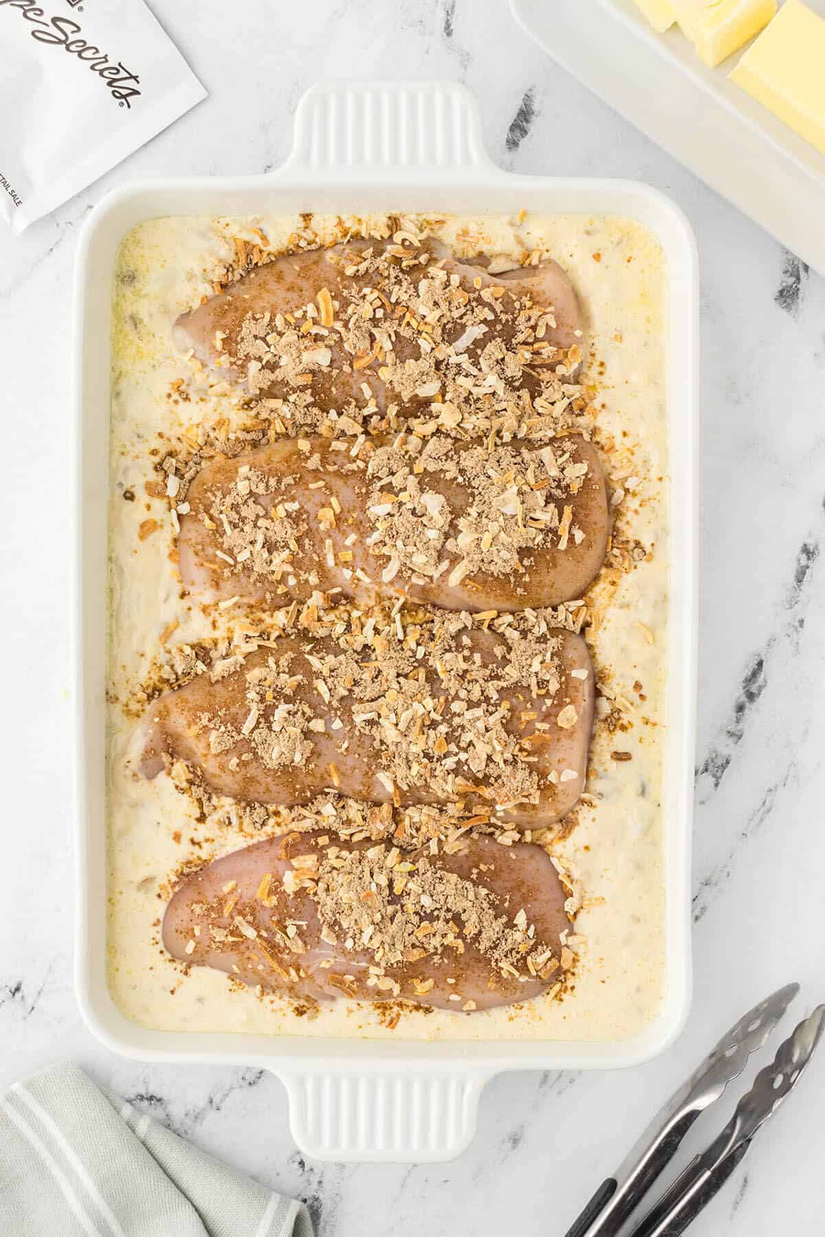 Chicken in a casserole dish topped with french onion soup mixture ready to pop in the oven.