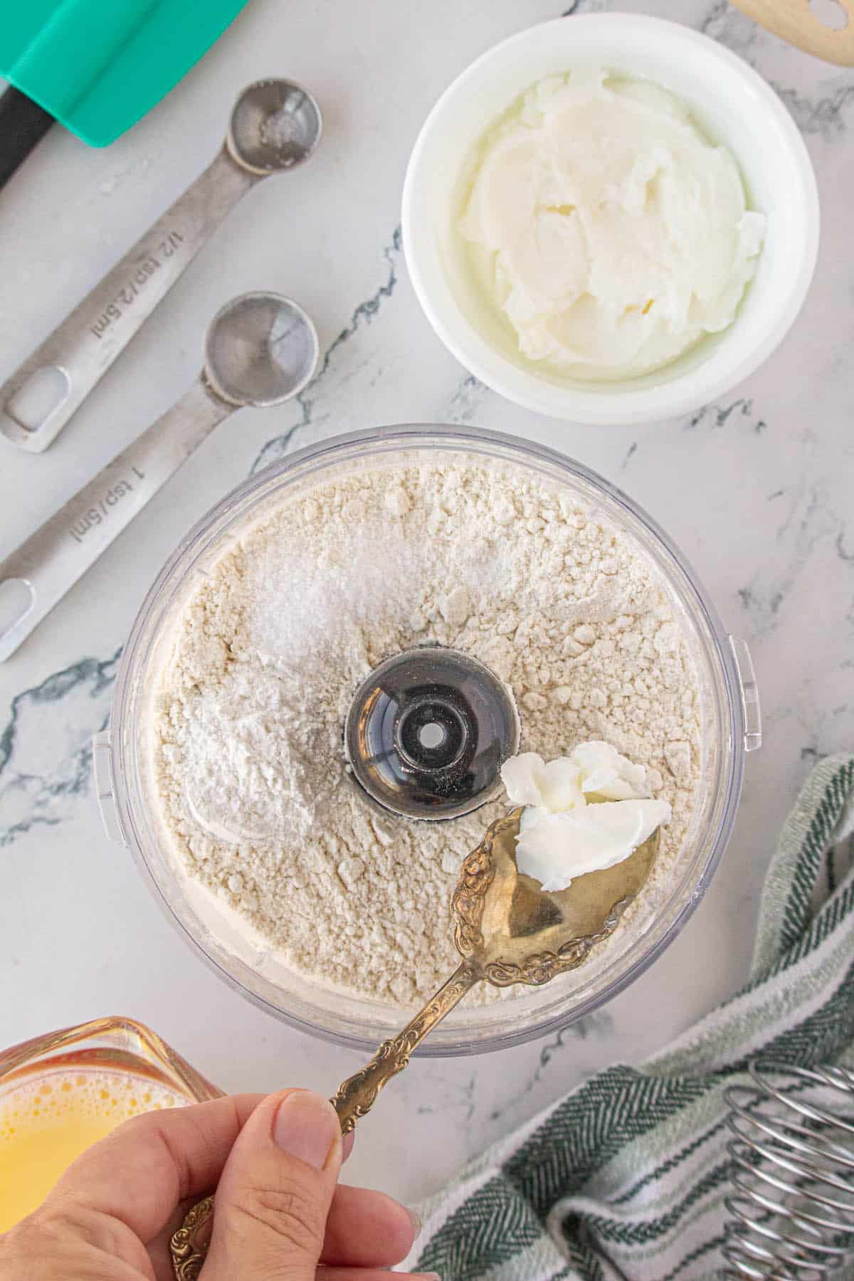 Shortening being added to a food processor filled with flour.