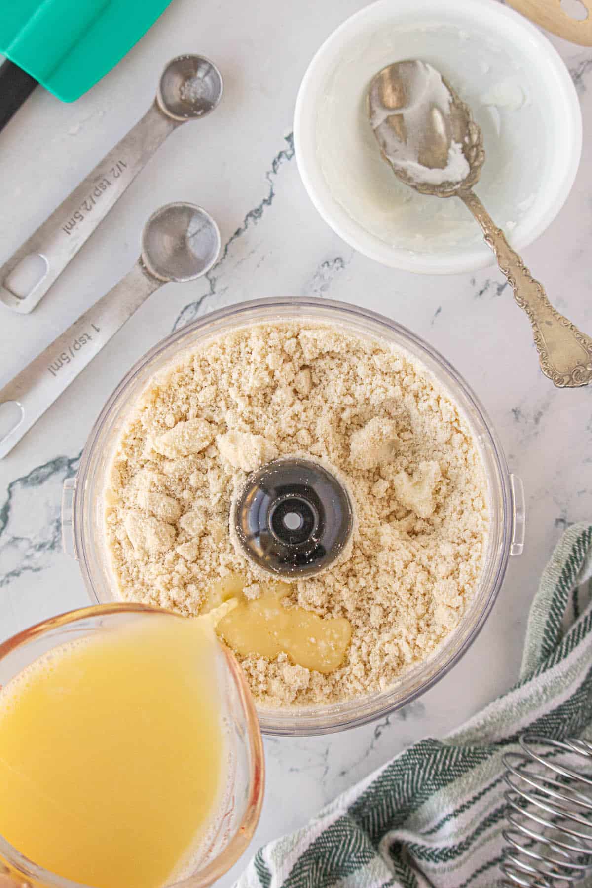 An egg mixture being poured into a flour mixture in a food processor.