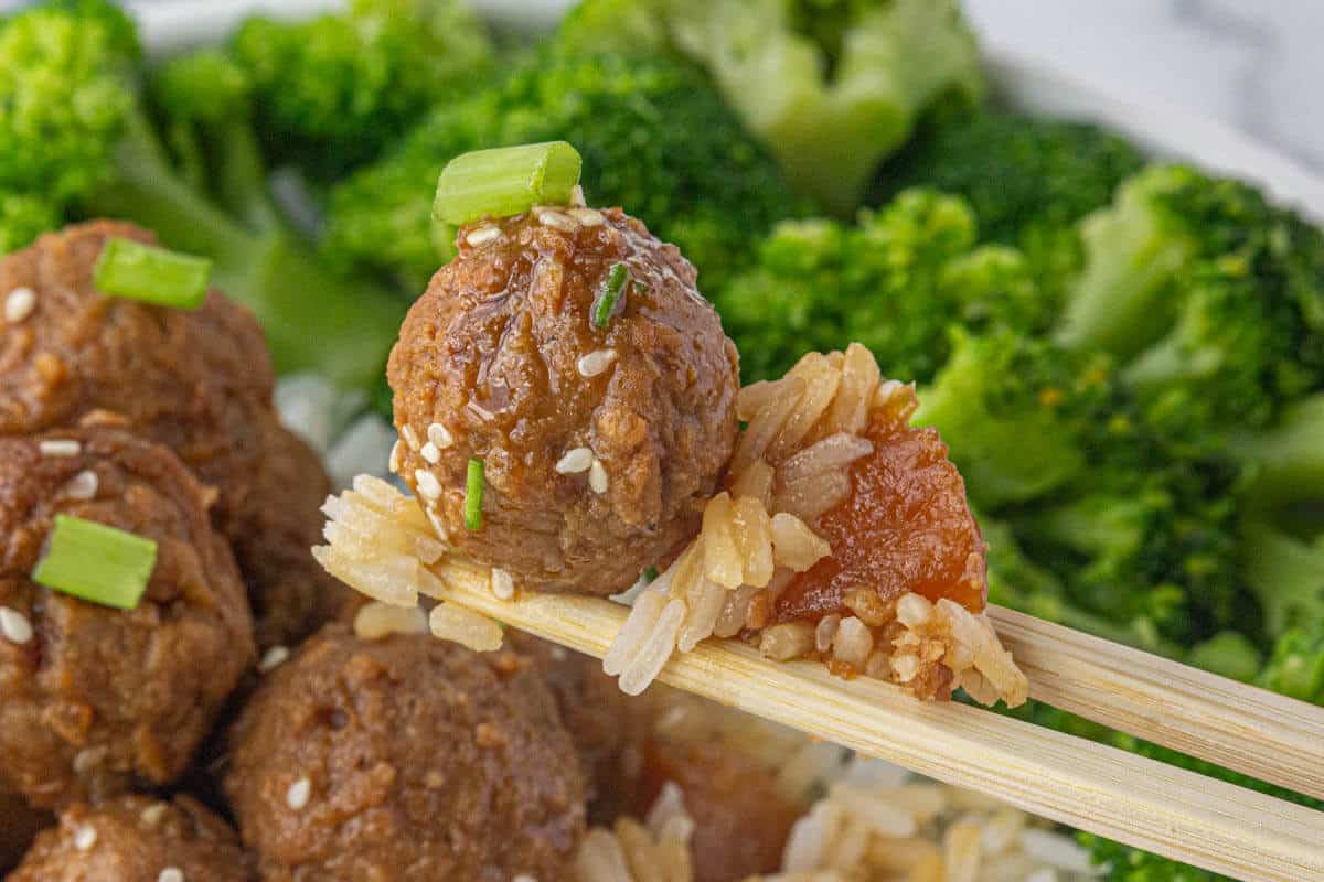 Chopsticks holding an Asian meatball, rice, and pineapple.