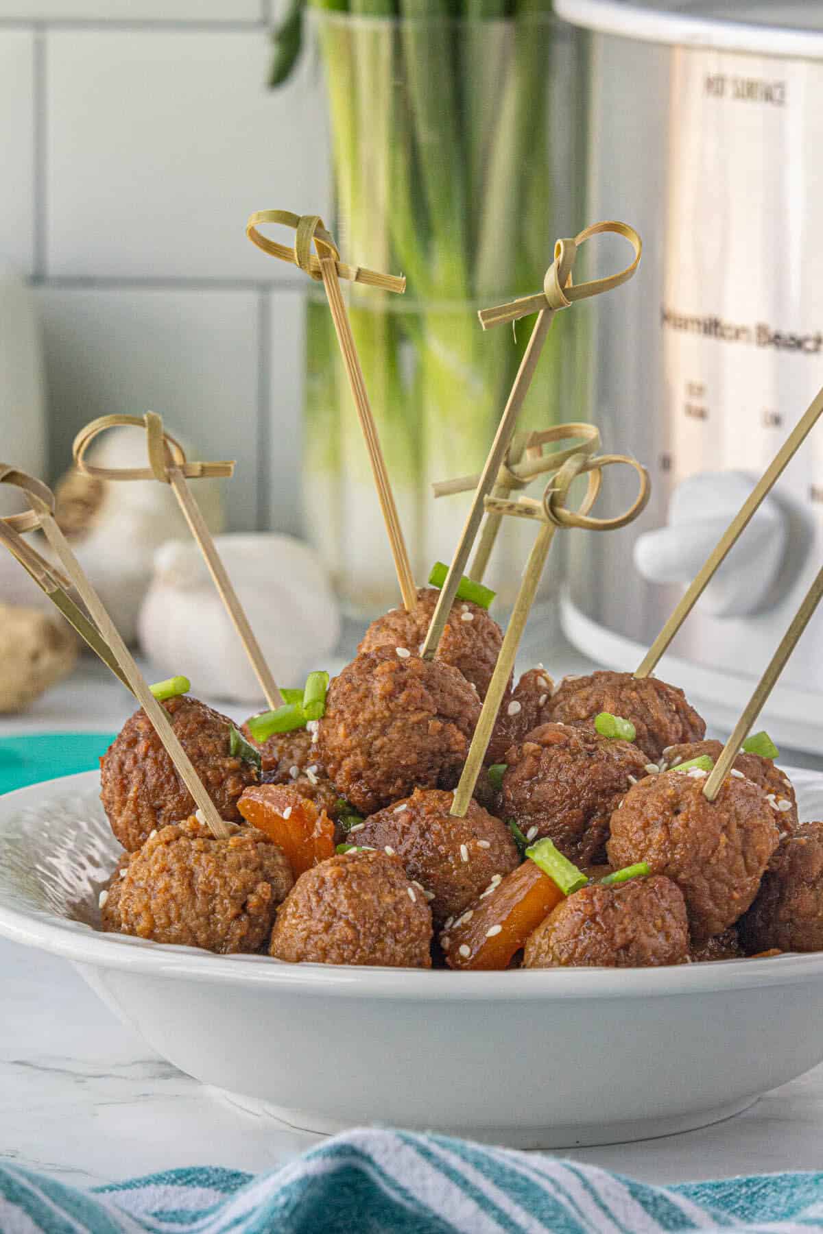 A bowl filled with teriyaki meatball appetizers. Toothpicks have skewered several of the meatballs to make serving easy.