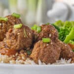 Crockpot teriyaki meatballs over rice, garnished with sesame seeds and sliced green onions.