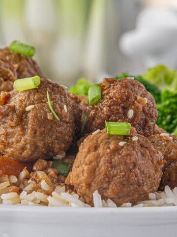 Crockpot teriyaki meatballs over rice, garnished with sesame seeds and sliced green onions.