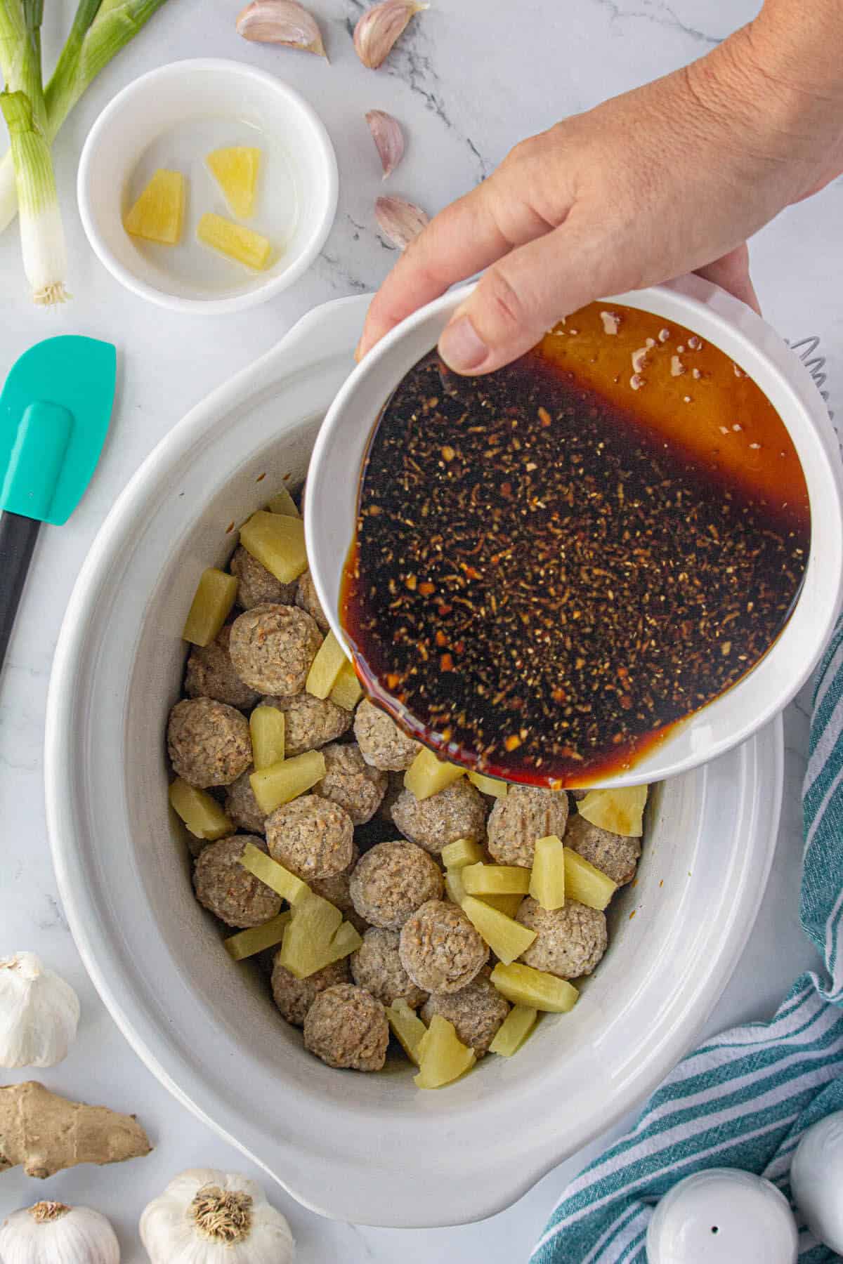 Sauce being poured into the crockpot over the meatballs.