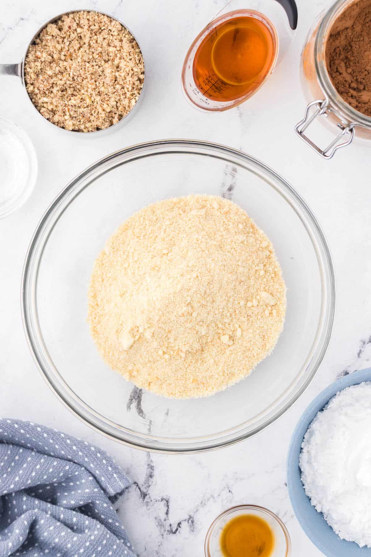 Pulverized cookie crumbs in a bowl, surrounded by the remaining ingredients to make bourbon balls.