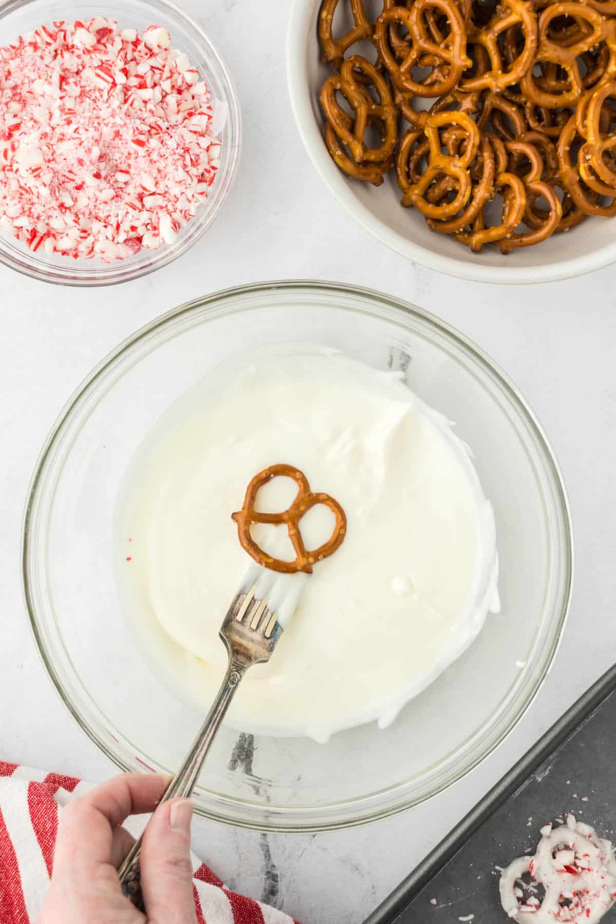 A pretzel being dipped into a bowl filled with melted white chocolate.