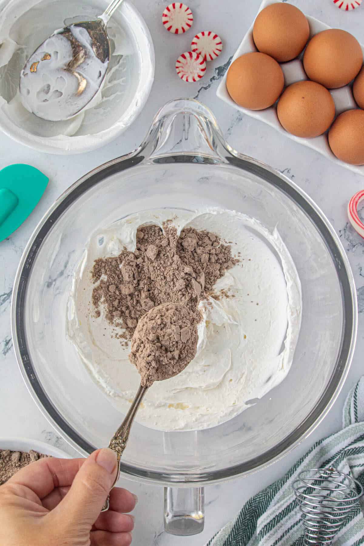 Cream cheese and Cool Whip in a mixing bowl. Chocolate cake mix is being added to the bowl.