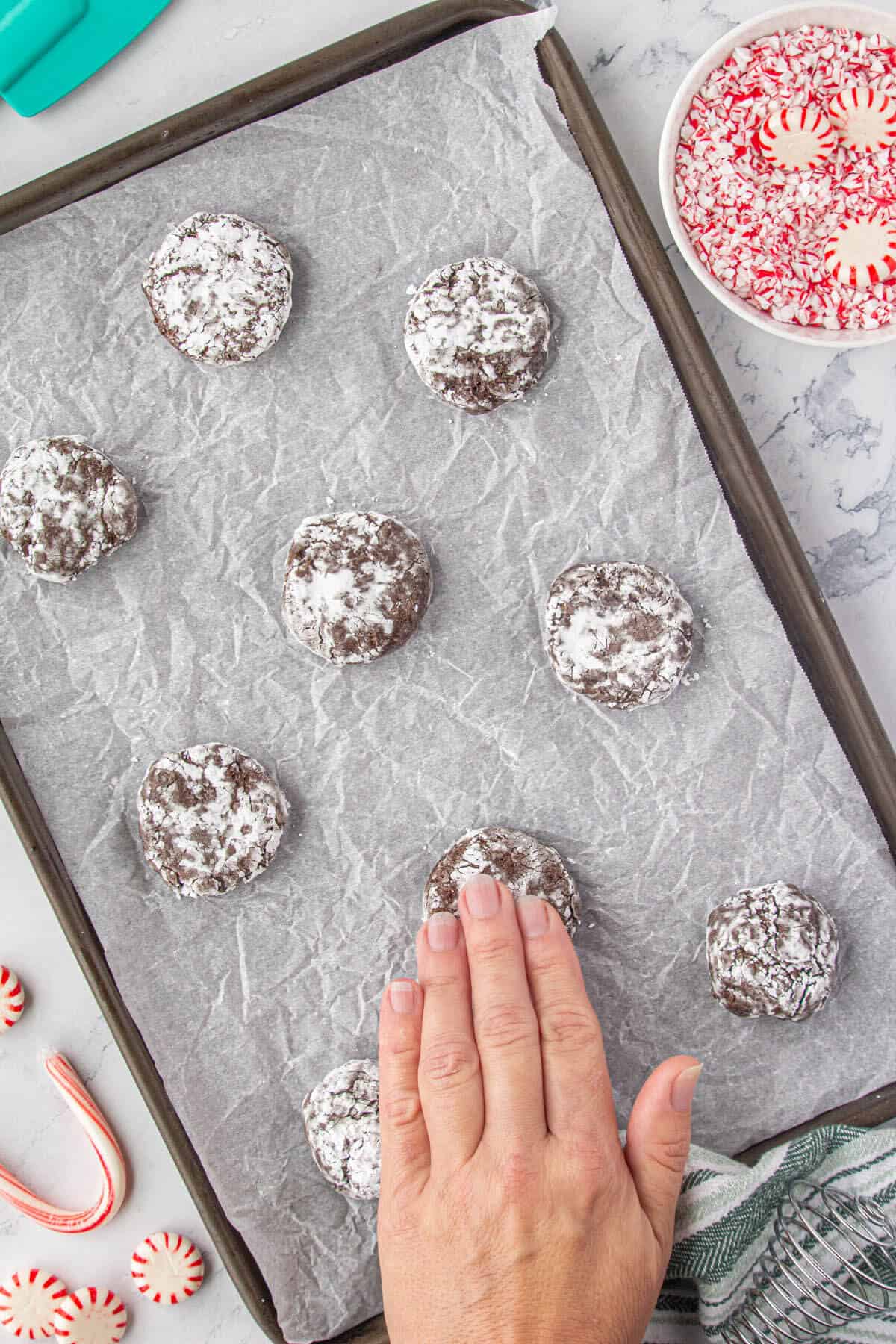 Unbaked cookies on a baking sheet. The dough is being lightly flattened.