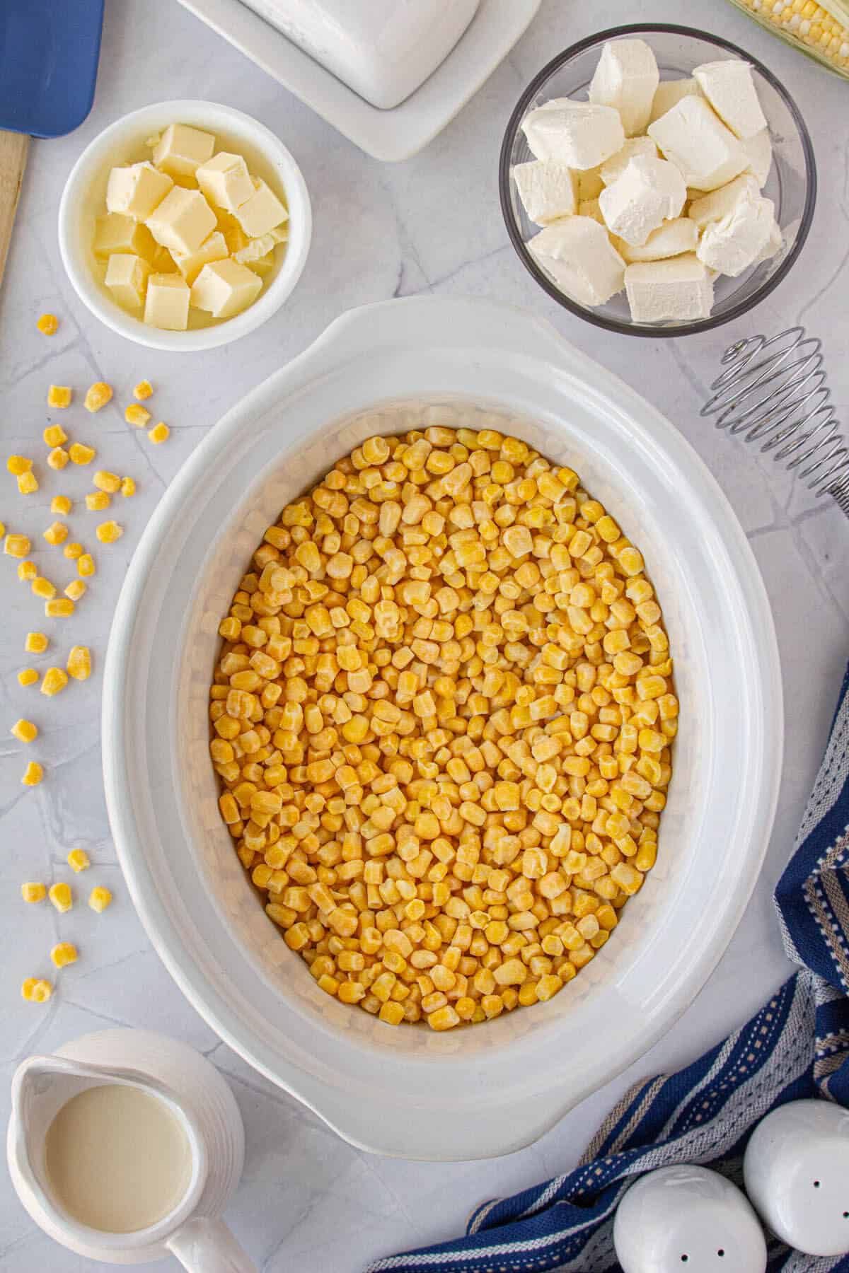 Corn in a crockpot surrounded by the rest of the recipe ingredients.