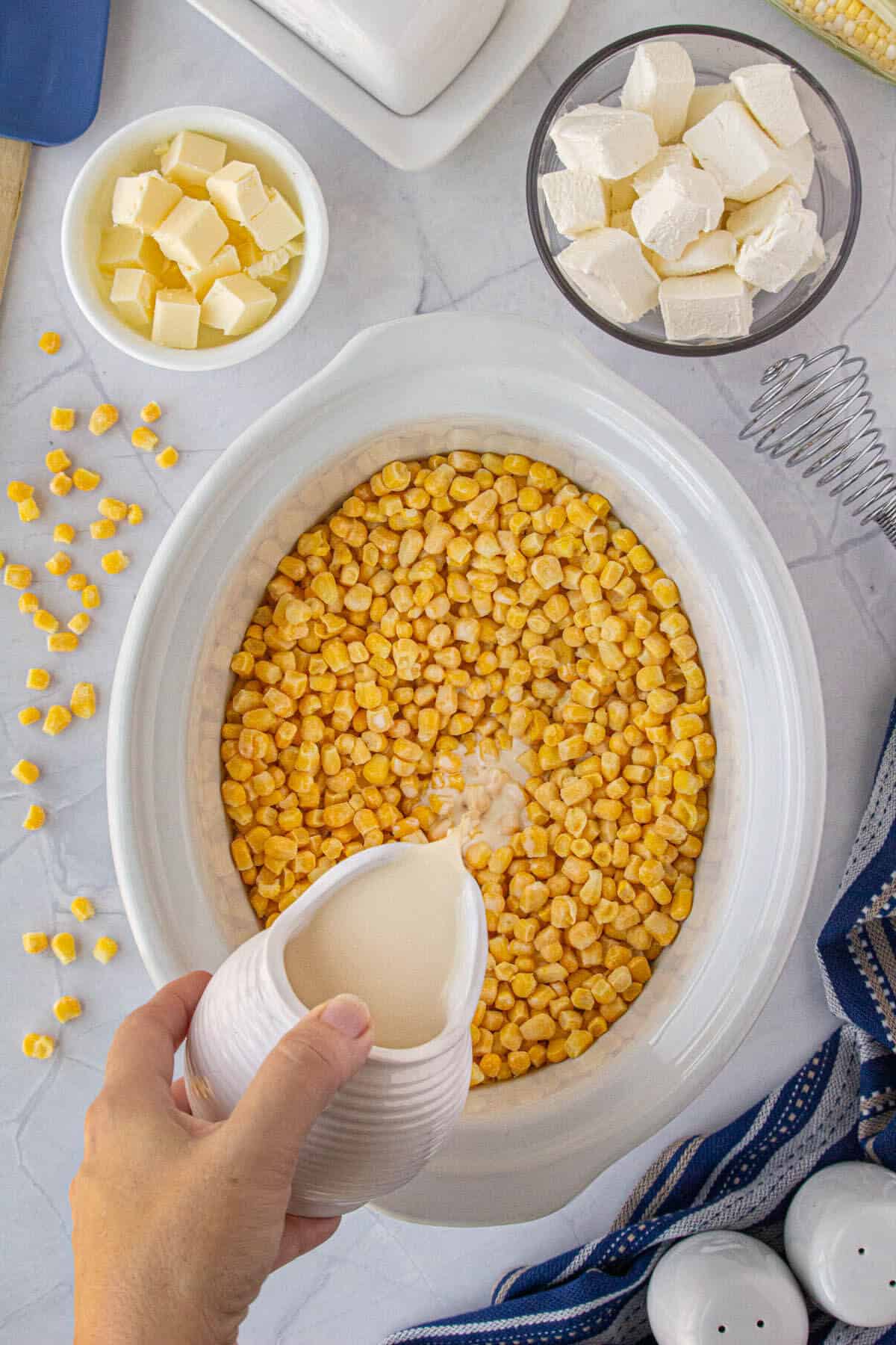 Cream pouring into the crockpot with the corn.