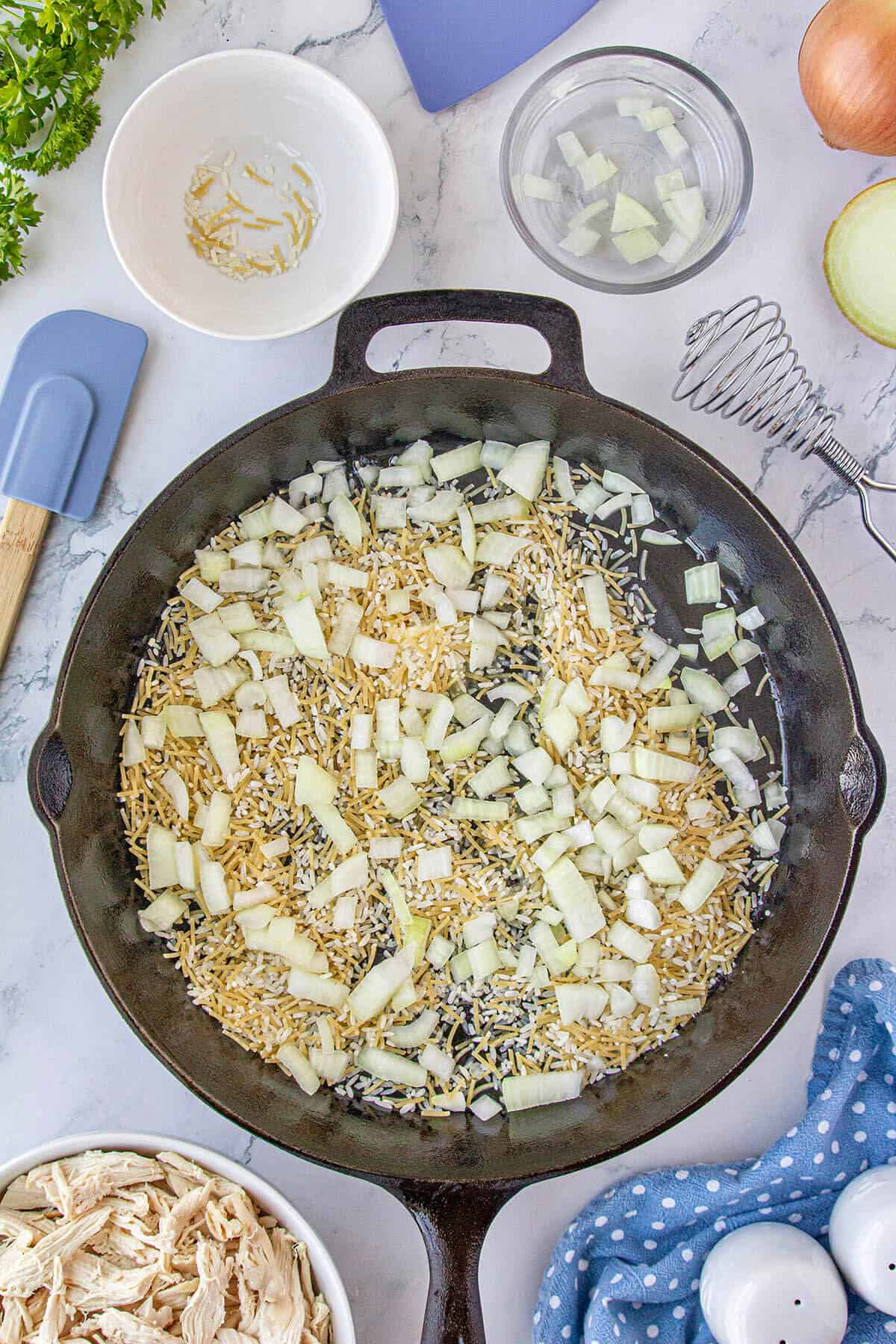 Rice a Roni and onions being sauteed in a skillet.