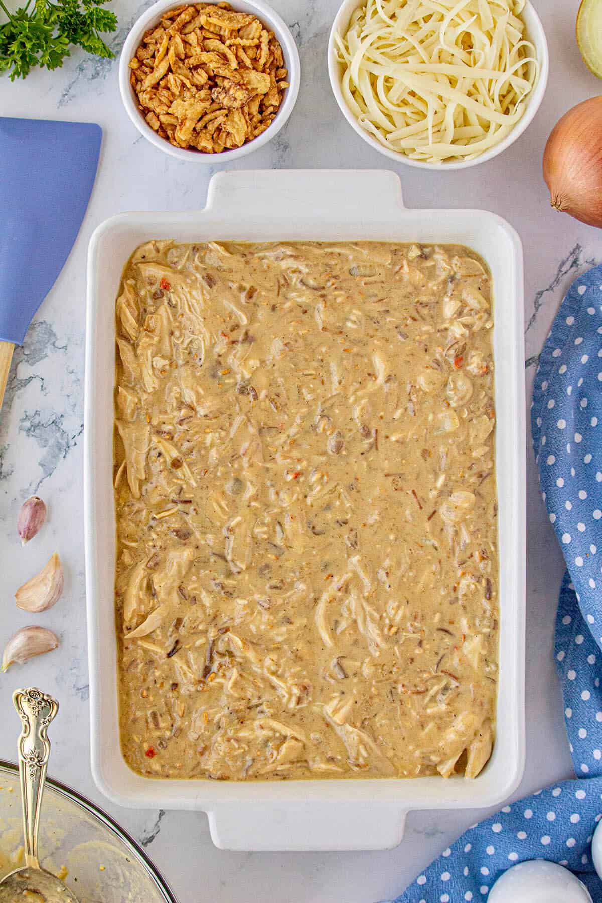 Chicken mixture being spooned into a casserole dish.