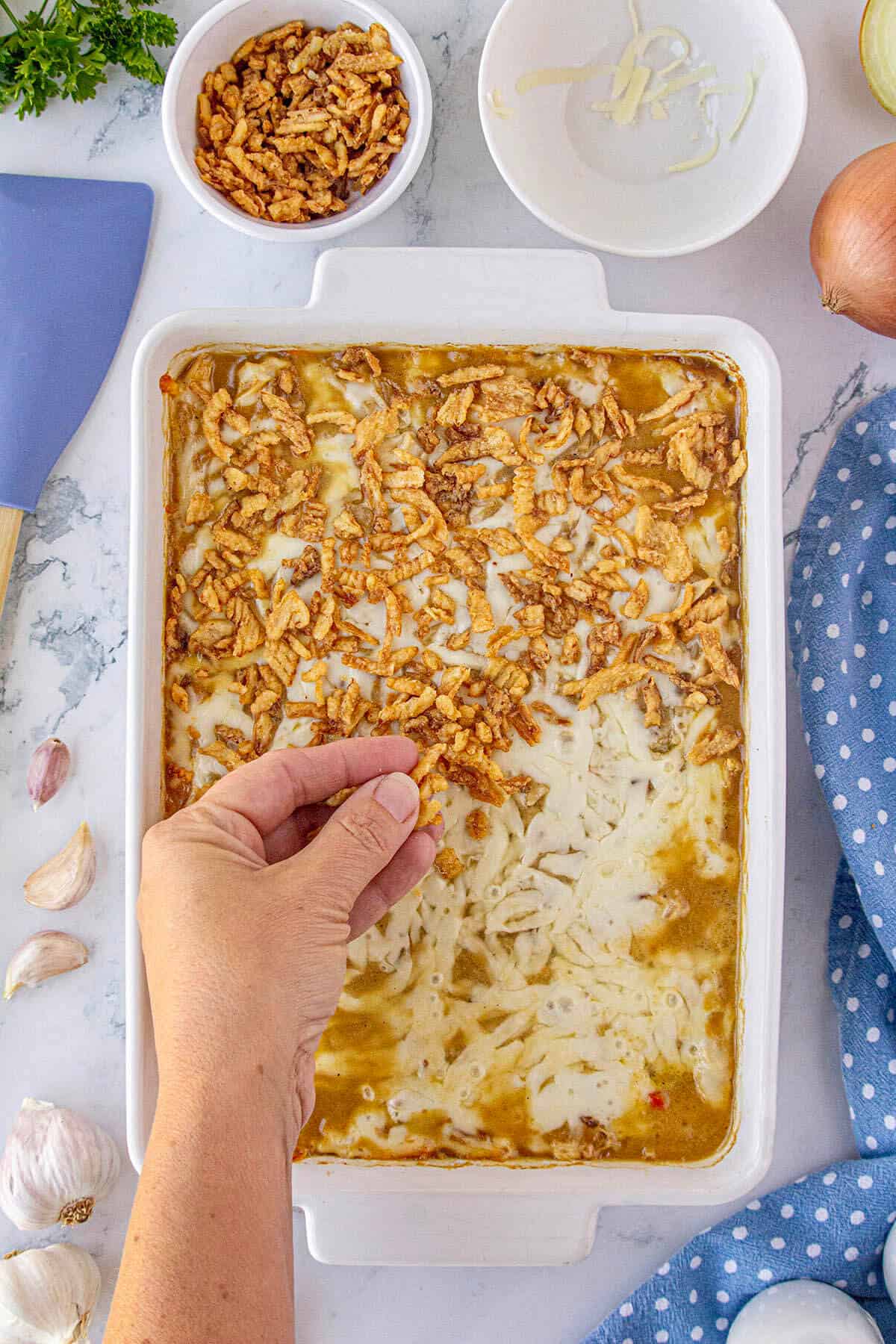 Hot casserole being topped with French fried onions before going back into the oven.