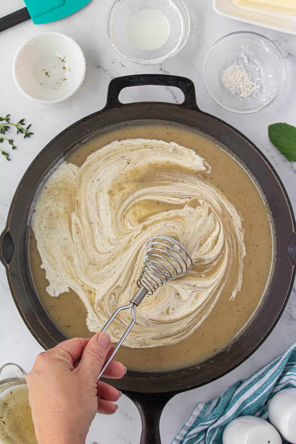 Milk whisked into gravy in a skillet.