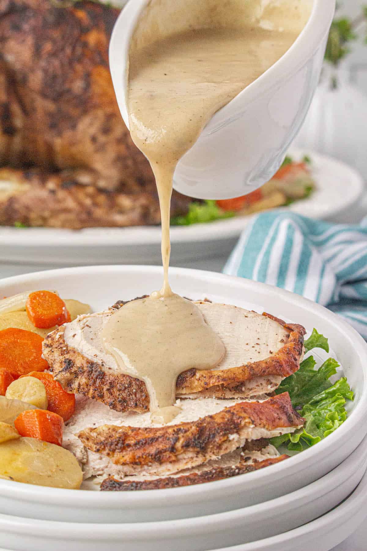 Thick, rich gravy pouring over slices of turkey on a plate.